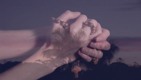 animation of landscape over caucasian woman's hands with rosary