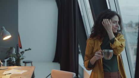 businesswoman holding tea and looking through window in office