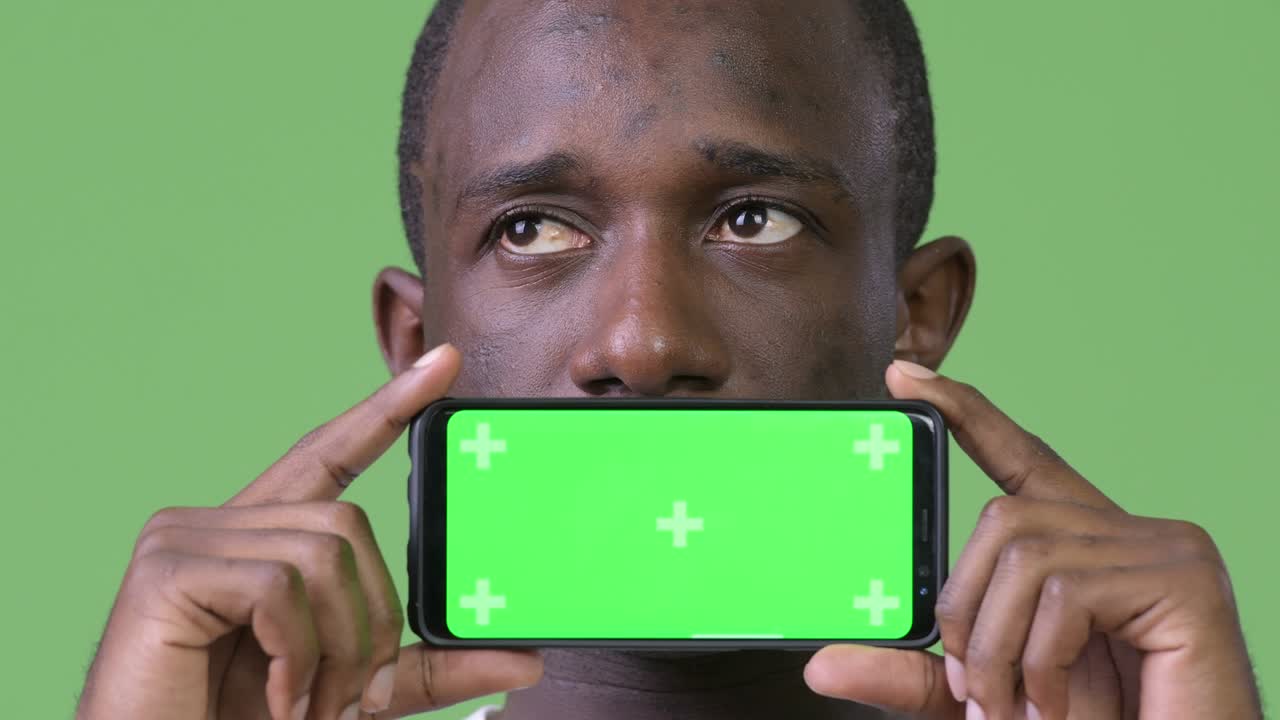 Jovem homem africano pensando enquanto mostra o celular
