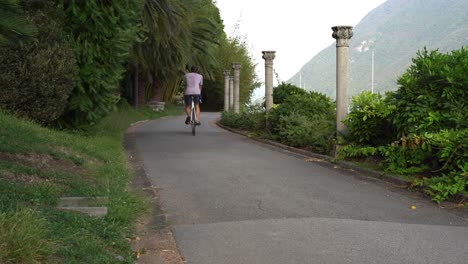 Guy-drives-a-single-speed-bicycle-in-his-beautiful-garden-hallway-surrounded-by-green-nature-and-mountains