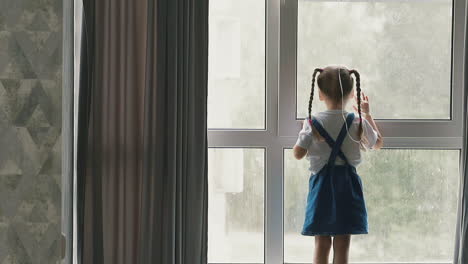 little girl stands near window staring