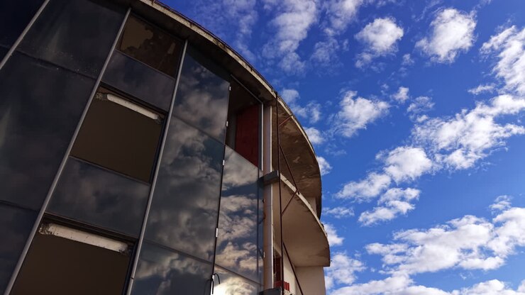 Sali lungo la facciata in vetro dell'edificio cilindrico con finestre in vetro colorato. Cielo azzurro con nuvole soffici sullo sfondo. Vista dal basso.