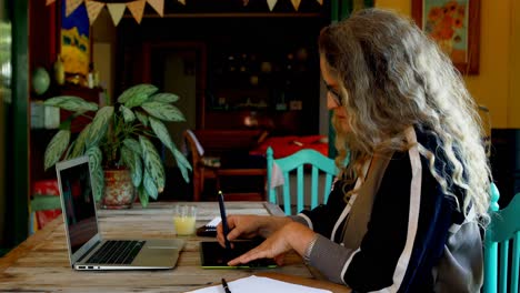 mujer madura tomando jugo mientras usa tableta gráfica 4k