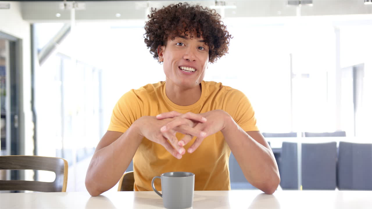 Waving hand, man sitting at table with coffee mug, smiling at camera