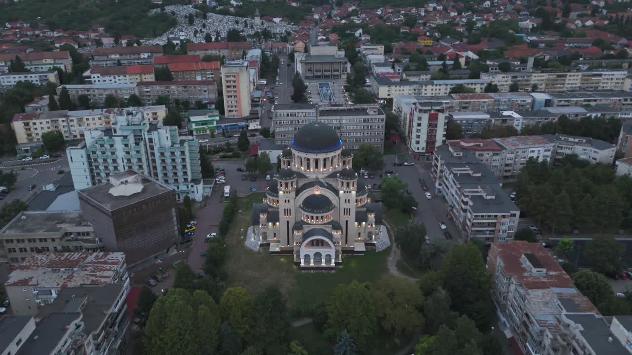 Aerial Orbital approach around Catedrala Adormirea Maicii Domnului in Deva, revealing the illuminated cathedral and its many cupolas glowing in the dark