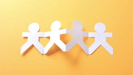 close up of people holding hands made of white paper on yellow background with copy space