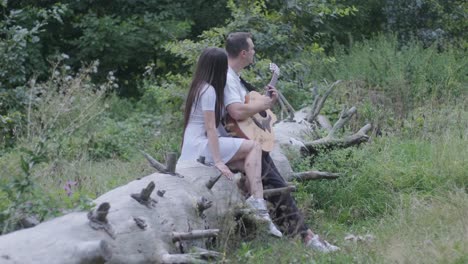 couple sitting on a tree trunk playing guitar in a forest