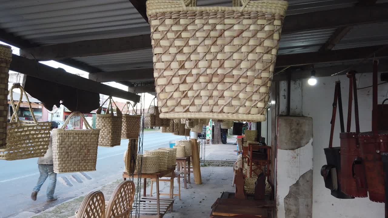 close shot of a shop selling handbags and mate drink woven in light brown wicker in an avenue with trucks driving