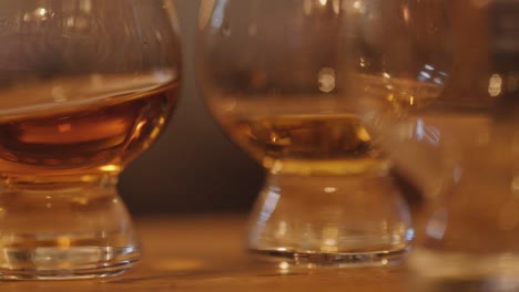 two whiskey glasses with amber liquid sit on a wooden bar, warm ambient lighting, shallow depth of field, and slow lateral camera movement