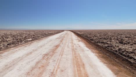 an aerial drone shot of a dirt road crossing the desert and a salt flat covered in salt and saltpeter in the atacama desert, filmed in broad daylight.