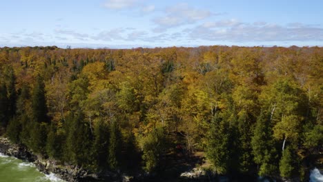 El-Dron-Vuela-Lejos-Del-Bosque-De-Otoño,-Revela-Aguas-Agitadas-Que-Se-Estrellan-En-La-Costa