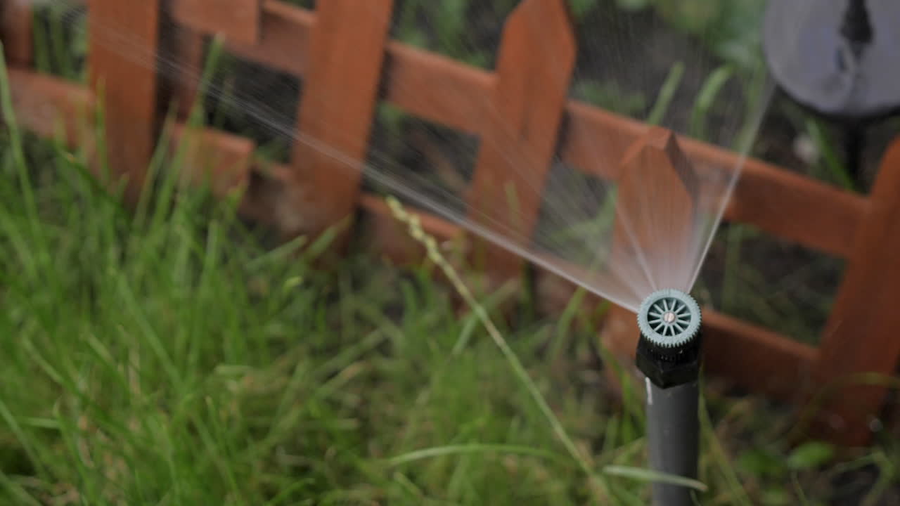 Spruzzo dell'irrigatore in cima a un'asta montante che irriga un giardino circondato da prato verde.