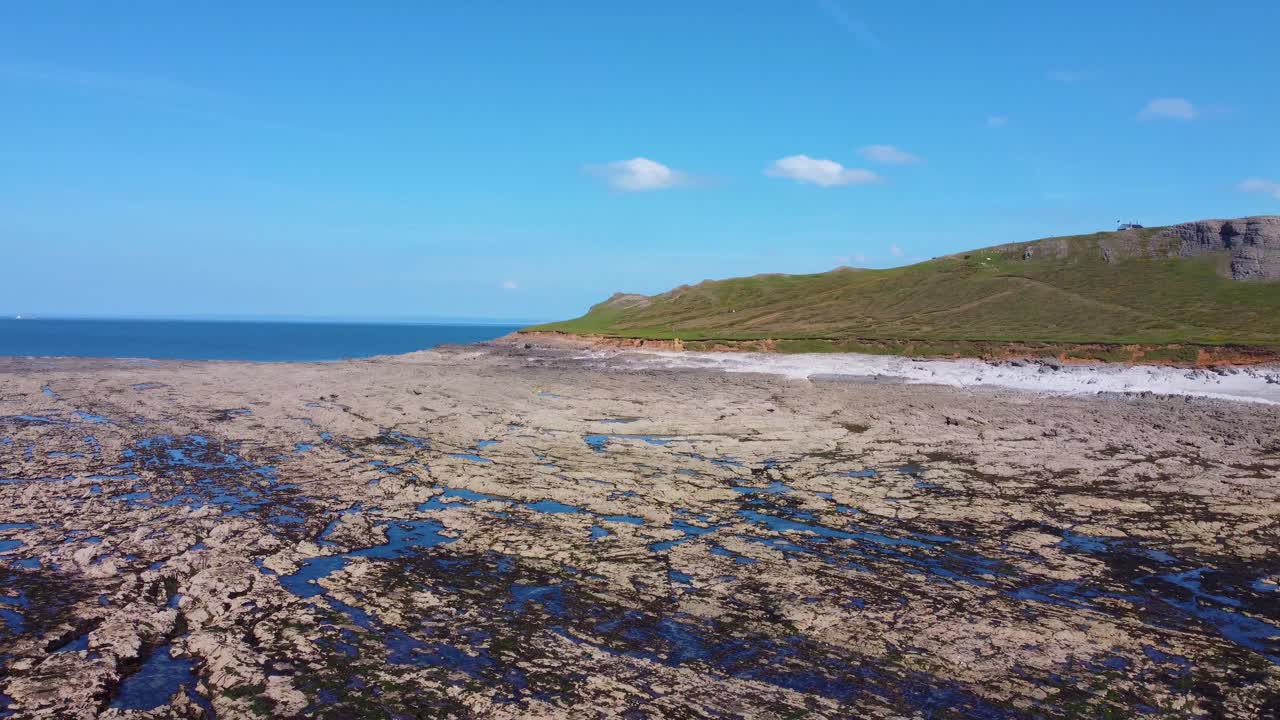 Turning Aerial View of Rock Pools in Rhossili with Worm's Head Landmark with Blue Sky Reflecting and Scattered Clouds and Cliffs. Nature Ocean Drone Footage.