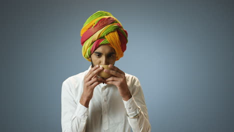 young cheerful indian man in traditional clothes and turban drinking tea from a cup