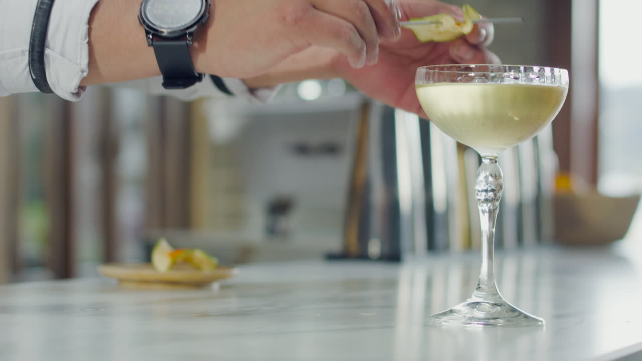 Close-up of a bartender placing a garnish on a cocktail glass at a modern bar. Ideal for food and mixology content