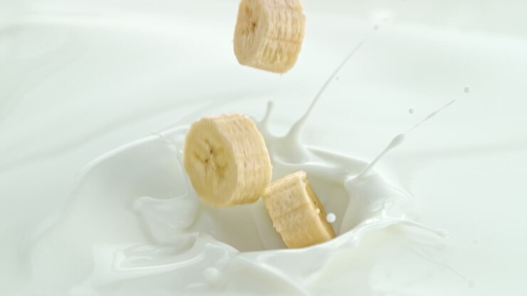 trozos de plátano cayendo en la leche cremosa haciendo salpicaduras giratorias en macro y cámara lenta