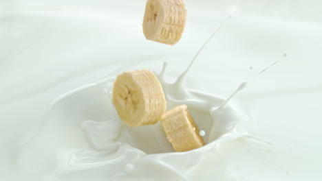 banana pieces falling into creamy milk making swirly splashes in macro and slow motion