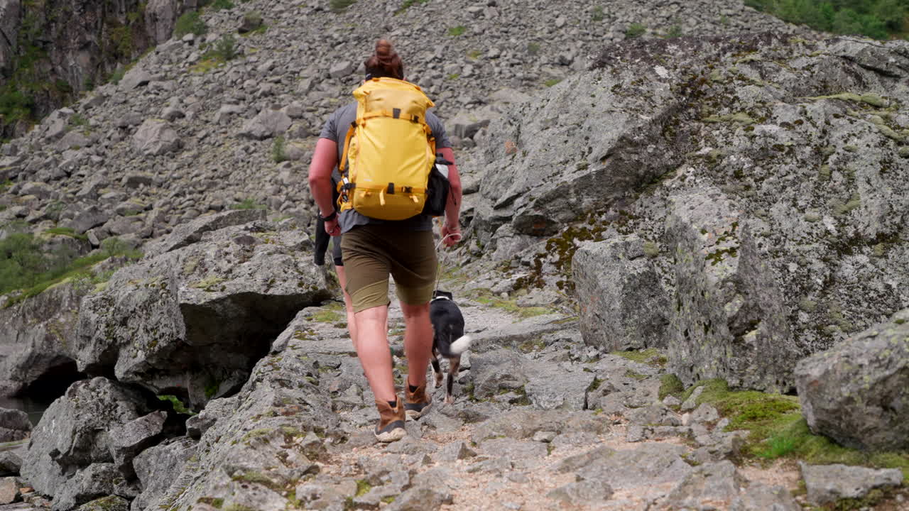 Explorer couple with dog hike on rocky trail past scree field on mountainside