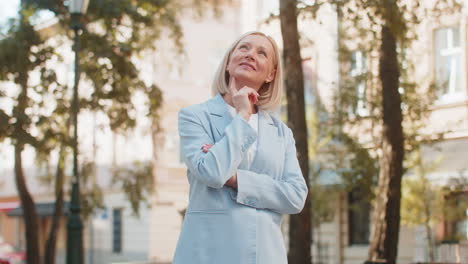 happy mature caucasian businesswoman on city street thinking of success dreaming feeling proud