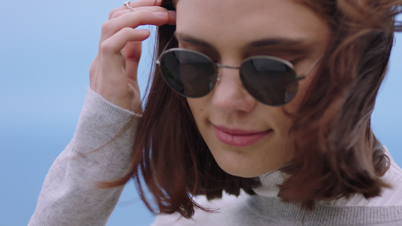 선글라스를 착용 한 아름다운 백인 여성 의 초상화 는 일몰 때 평화로운 해변 을 즐기고 있으며, 머리카락 을 가로질러  ⁇ 상적 으로 달리는 손 을 보고 있다