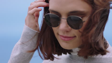 retrato de una hermosa mujer caucásica con gafas de sol disfrutando de una tranquila playa al atardecer buscando contemplativa corriendo la mano a través del cabello