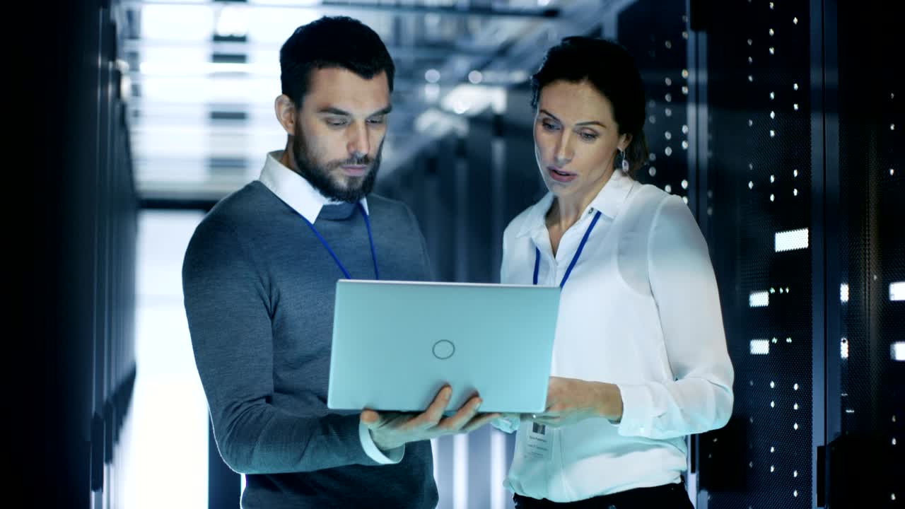 el especialista masculino muestra información en una computadora portátil al técnico de servidores femenino. están de pie en el centro de datos.