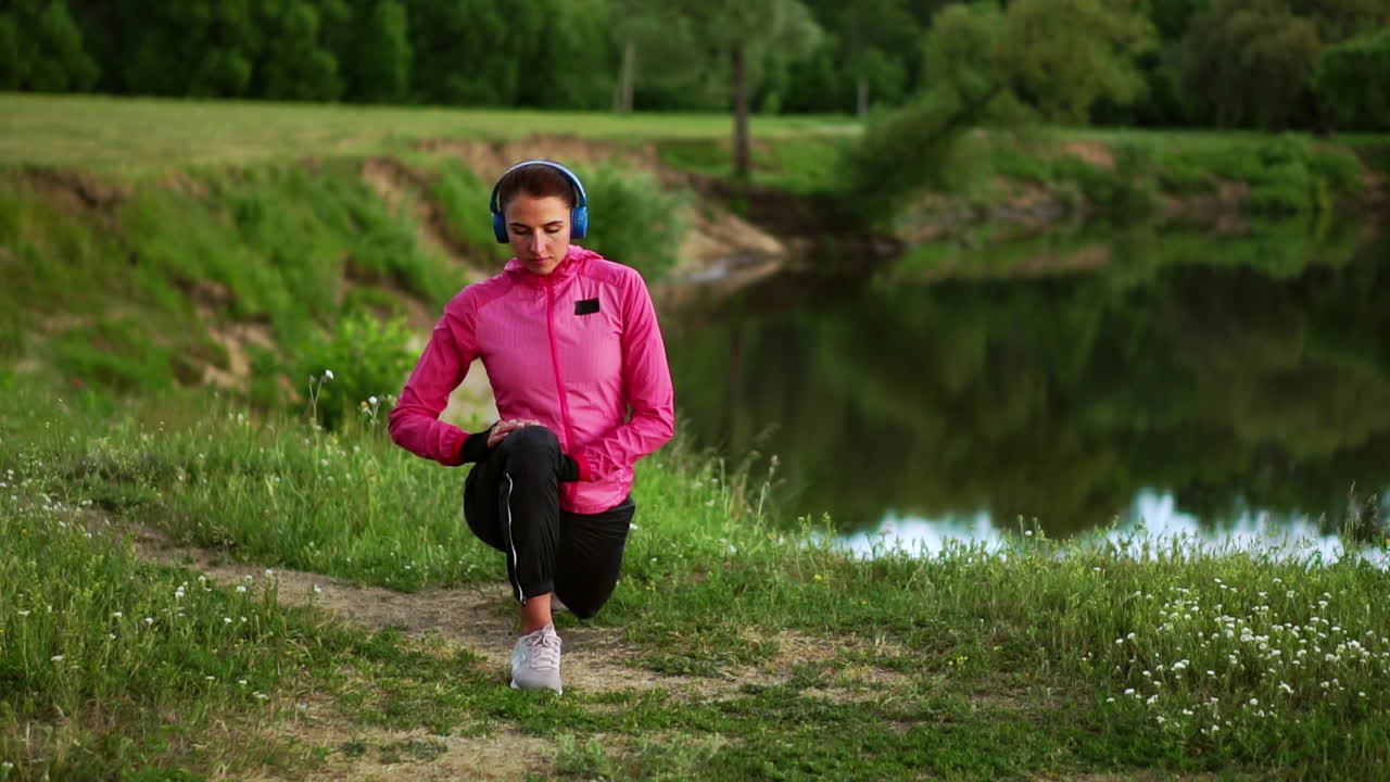 A girl in a pink jacket is preparing for a run warm up and listen to music in headphones through the phone