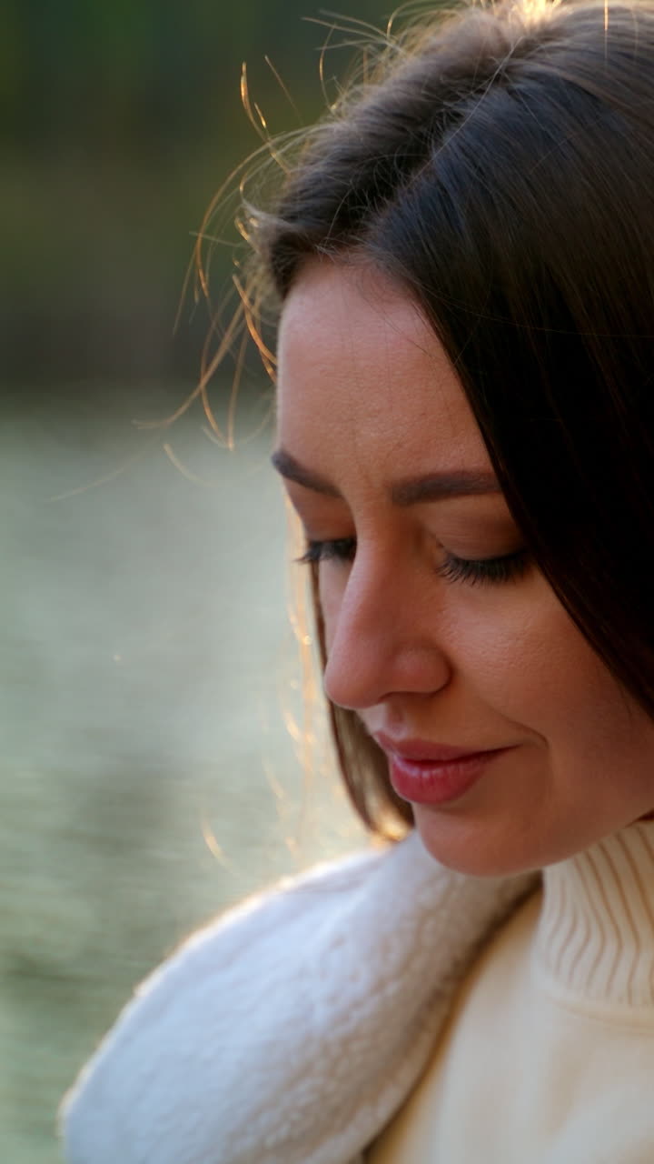 Relaxed Caucasian lady with long hair standing outdoors in the rays of sun. Close up. Attractive lady using phone near the river.