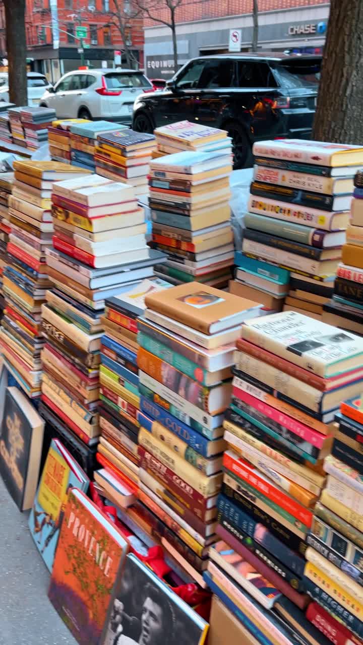 New York, USA, 11. Mai 2025: Stapel gebrauchter Bücher zum Verkauf auf einem Bürgersteig in der Stadt. Vertikale Stapel von Hardcover- und Taschenbüchern, die im Freien auf einem Gehweg nahe dem Straßenverkehr bei Tageslicht ausgestellt sind.