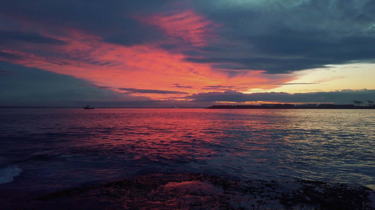 Distant boat travels on horizon during fiery red sunset near coastal waters
