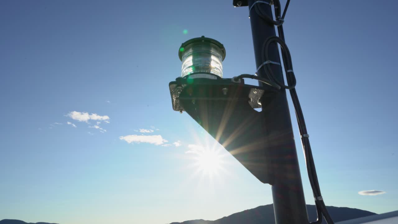Ships lantern with blue sky and strong sunlight behind - Lantern close to camera showing cables and bracket - Lens flares on camera rotating around lantern