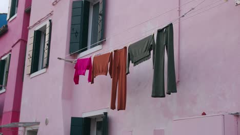 Pintoresca-Escena-De-La-Isla-De-Burano,-Venecia,-Que-Muestra-Un-Edificio-De-Color-Rosa-Pastel-Con-Ropa-Tendida-A-Secar-En-Un-Tendedero,-Creando-Una-Atmósfera-Vibrante-Y-Encantadora