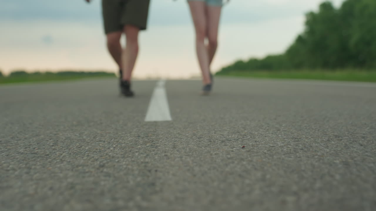 blurred lower legs of man and woman walking side by side along white road marking through rural open field at sunset evoking sense of journey motion connection outdoors freedom peaceful