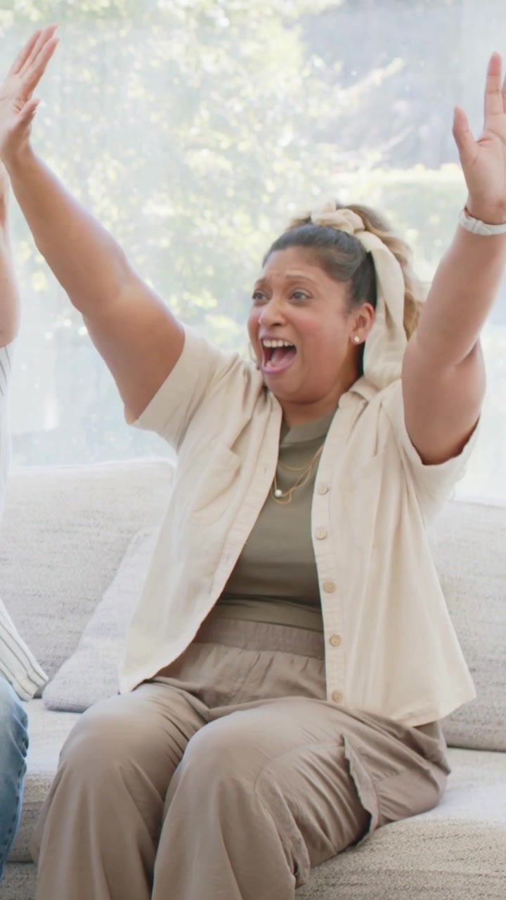 Woman sitting on sofa reacting to offscreen win, celebrating in marketing clip with confetti rising
