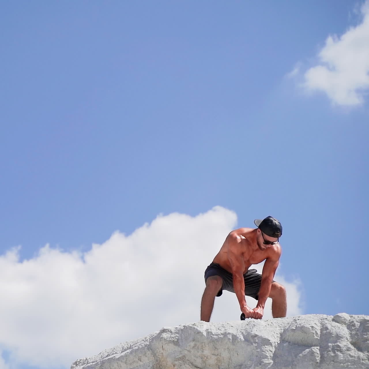 Healthy athlete taking up heavy kettlebell outdoors. Fitness training man lifting weight on the top of white mountain. Slow motion.