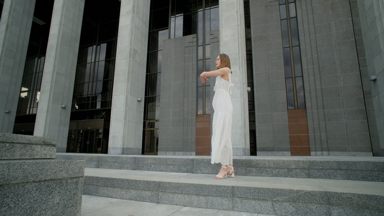 Woman Dancing in a White Dress in Front of a Modern Building