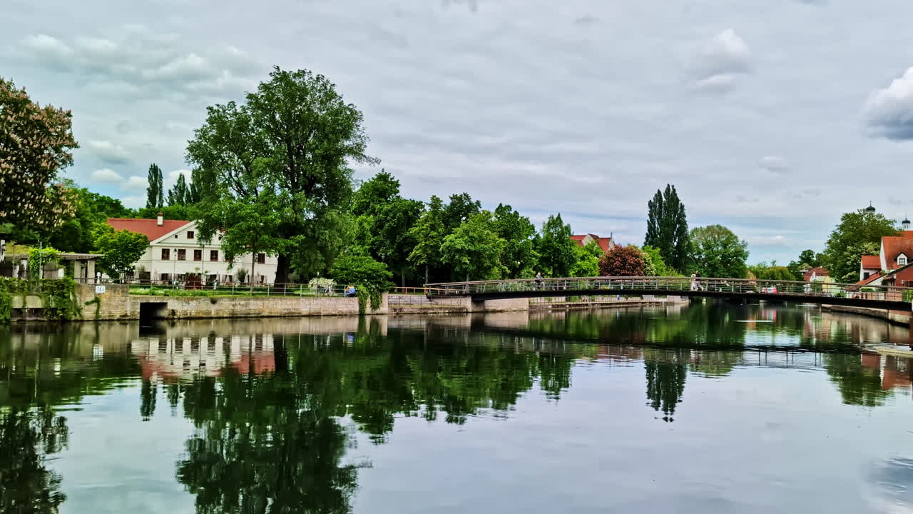 Calm river flowing through Landshut town with reflections and bridge on cloudy day
