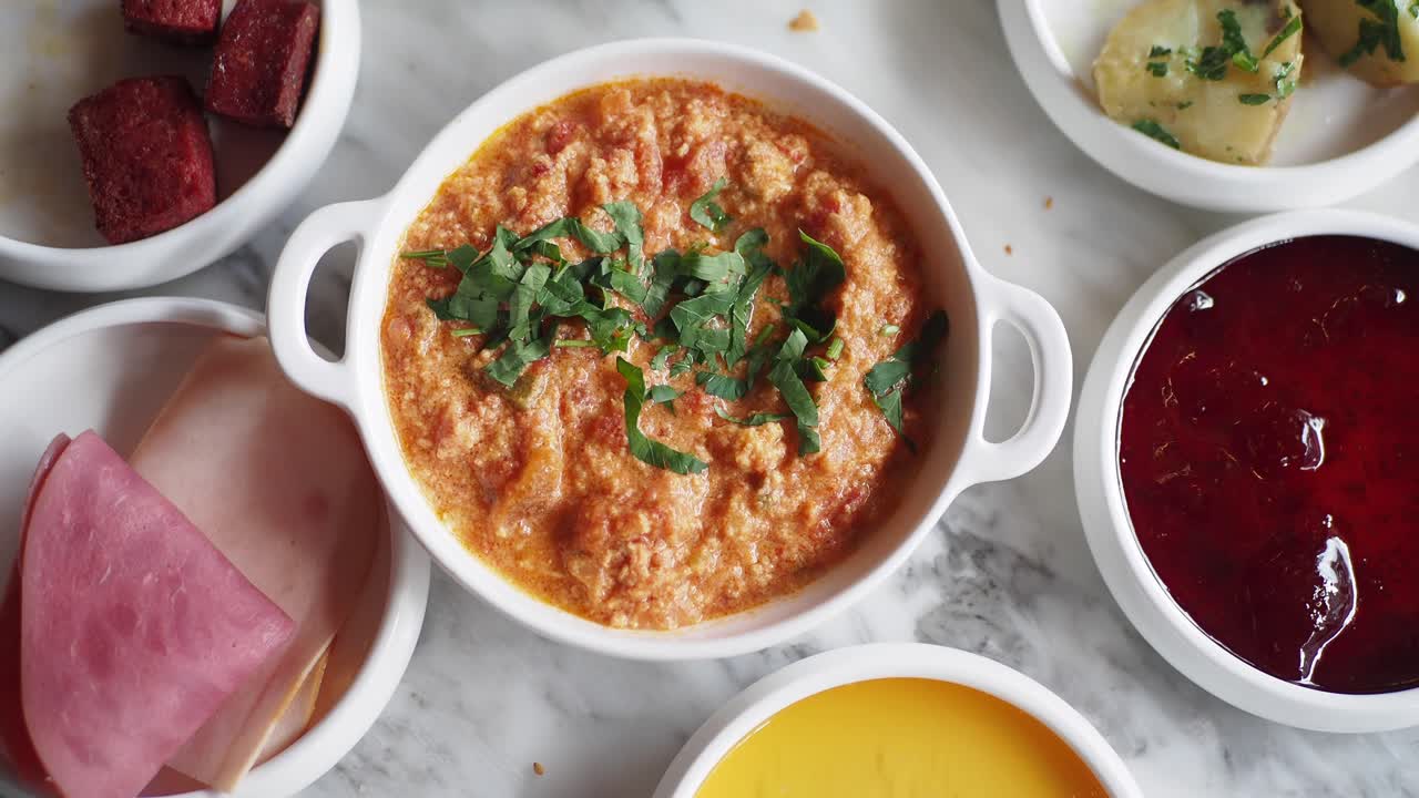 un desayuno turco con huevos revueltos, sucuk, jamón, queso, aceitunas y mermelada