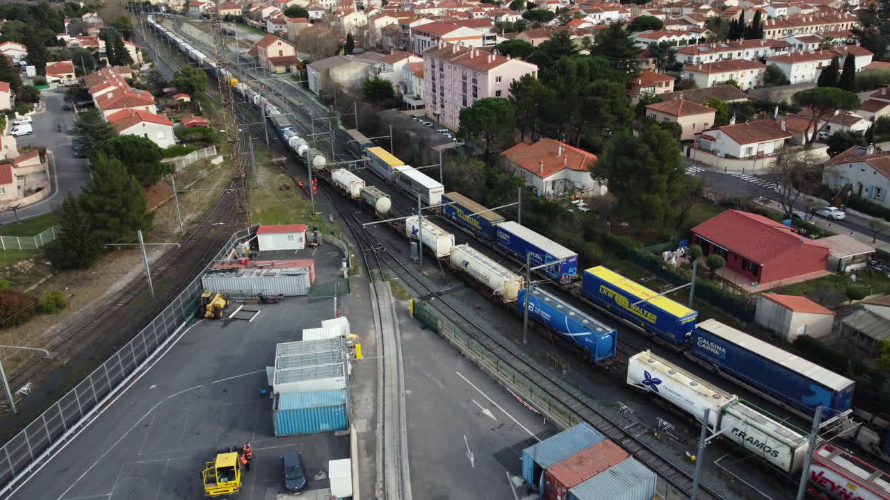 Aerial view of a freight train in a rail yard, with surrounding industrial area and residential buildings