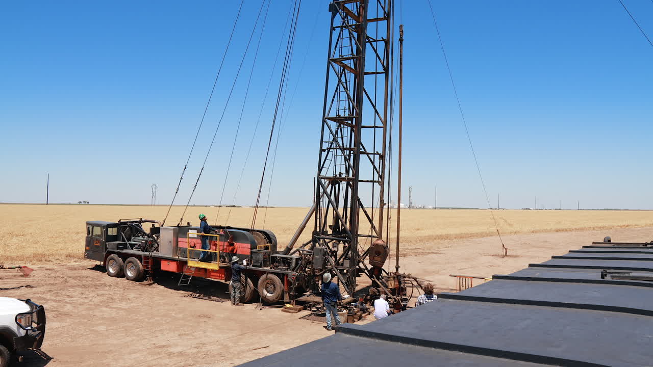 Workers wearing protective helmets stand at the truck with oil derrick. Men look up at the tower for drilling oil.