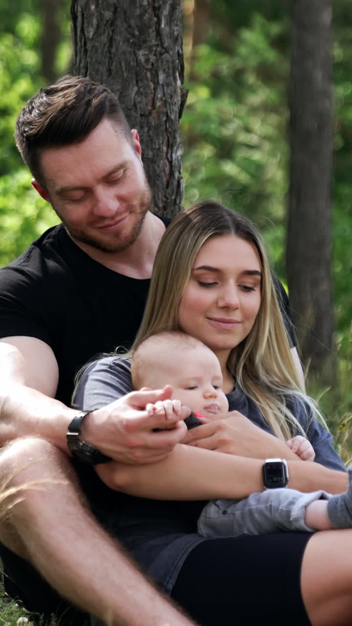 Man and woman sit in the nature with their adorable newborn. Caucasian family spending time in the forest. Vertical video