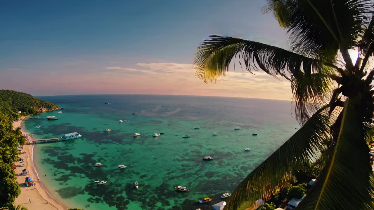 Aerial view of a tropical beach at sunset, showcasing turquoise waters and boats