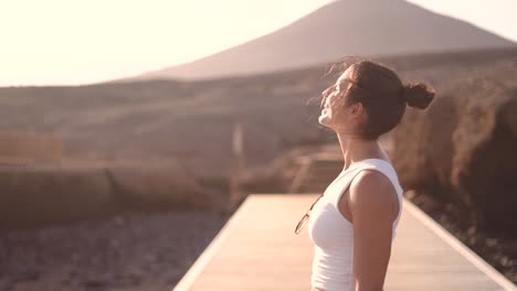 mujer linda en mesas de madera camino durante la puesta de sol contra la cordillera disfrutar del sol y el viento en cámara lenta