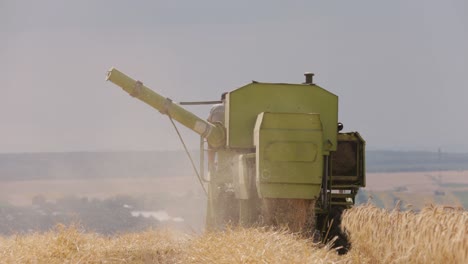 close up view of the rear of an old green combine harvester at work in a wheat field in slow motion