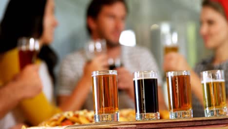 tres vasos de whisky en la mesa mientras los amigos tienen un vaso de cerveza en el fondo 4k
