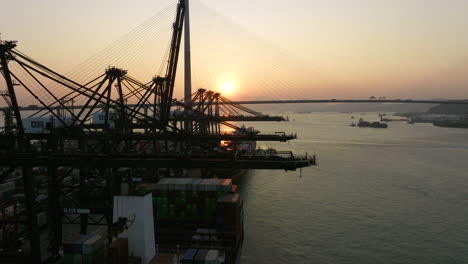 grúas de pórtico cargando y descargando contenedores en barcos amarrados con un gran puente colgante en el fondo durante la puesta de sol