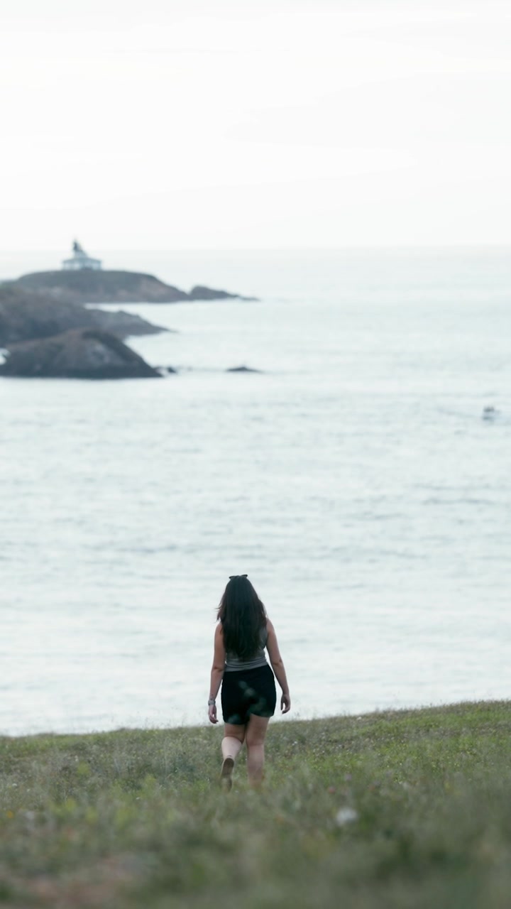 Young Woman Walking Through Grassy Field Toward Ocean
