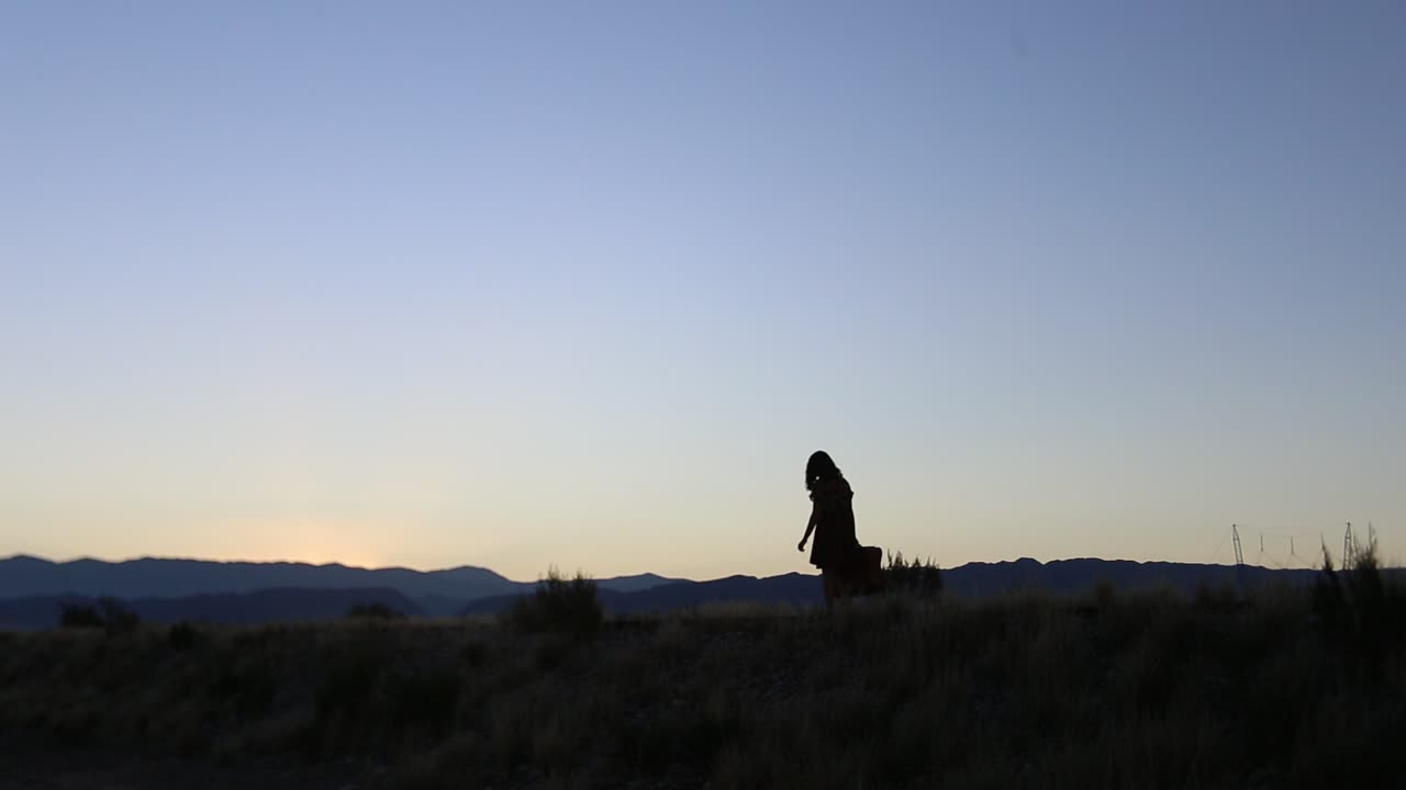 Silhouette of a Woman Walking at Sunset in a Desert Landscape