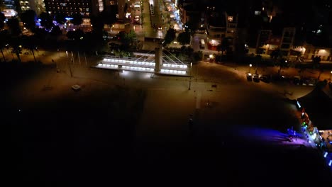 night-view-of-the-central-street-of-calella,-and-a-beach-bar-with-illuminated-buildings-and-cars-driving-along