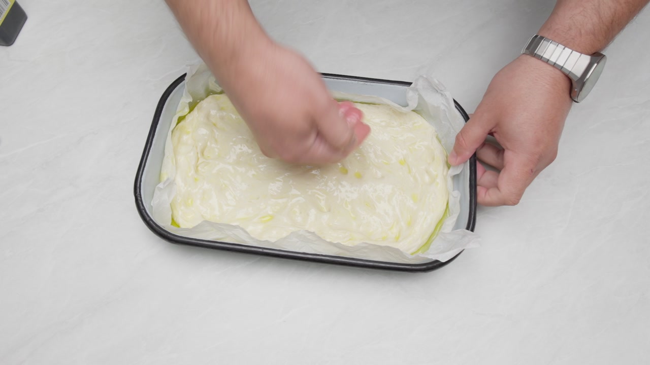 Top down view of olive oil spread by hand over focaccia dough